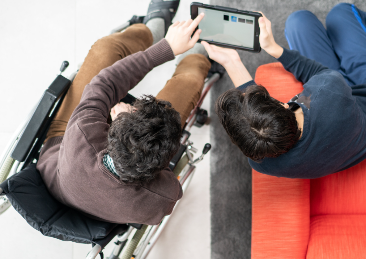 dos personas, una de ellas en silla de ruedas, usando conjuntamente una tablet