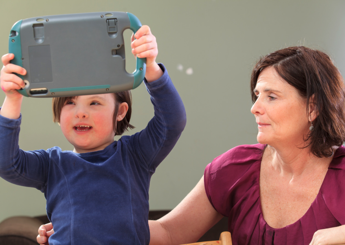 mujer sentada al lado de un niño con sindrome de down con un comunicador en las manos